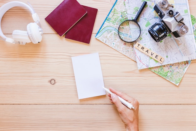 Free Photo a person writing on paper with traveler accessories on wooden background