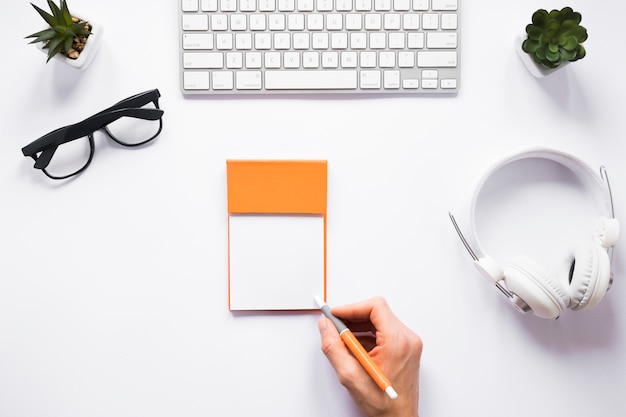 Free photo a person writing on sticky notes with pen on white workspace