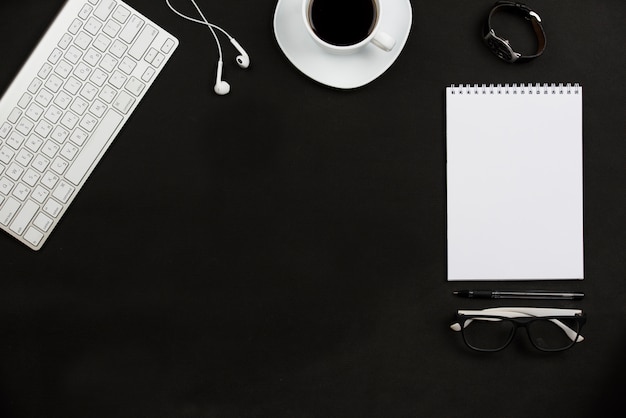 Personal accessories; coffee cup; earphone; eyeglasses and keyboard on black background