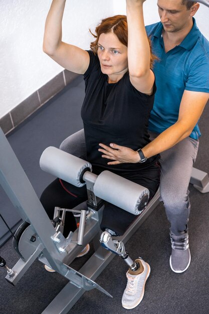 Personal trainer assisting woman with disabilities in her workout. Sports Rehab Centre with physiotherapists and patients working together towards healing.