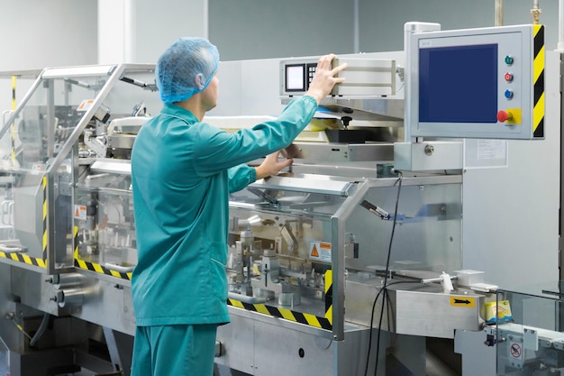 Pharmaceutical factory man worker in protective clothing operating production line in sterile environment