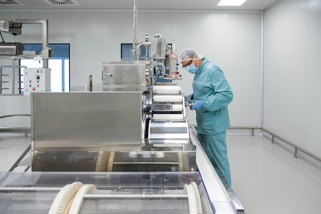 Free photo pharmacy industry factory man worker in protective clothing in sterile working conditions operating on pharmaceutical equipment