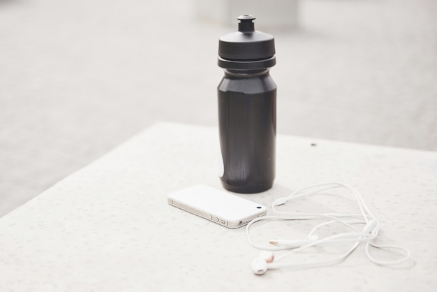 Phone headphones and a bottle of water in the open air. Accessories for running sports