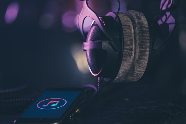 Phone with music icon and headphones on blurred background, music listening concept, copy space.