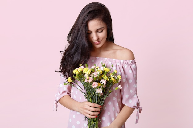 Photo of attractive brunette female model holds spring flowers, wears polka dot dress