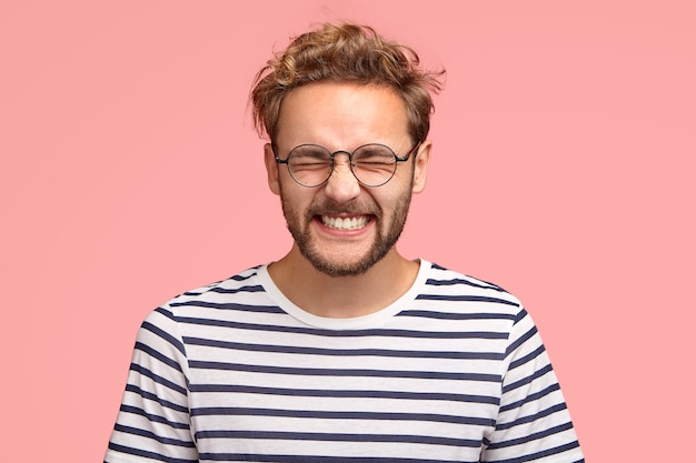 Free Photo photo of attractive cheerful man laughs positively at camera, keeps eyes closed