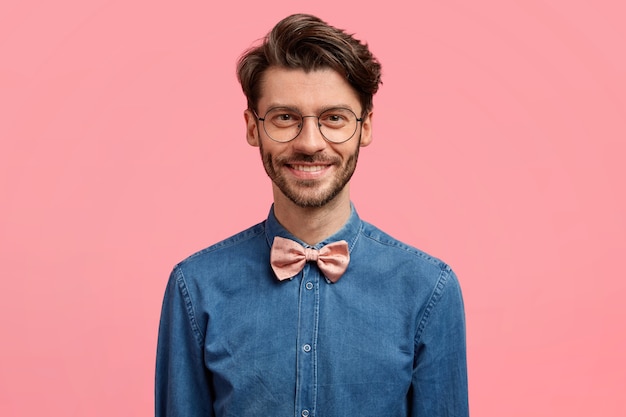 Free photo photo of attractive smiling man with trendy hairstyle, positive look, dressed in fashionable festive outfit, stands against pink wall