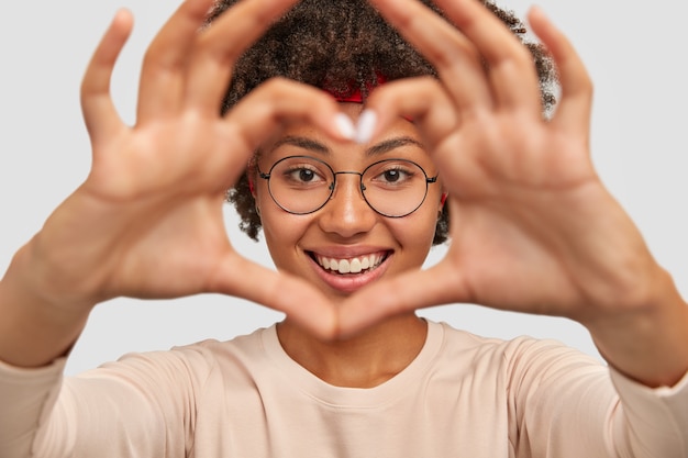 Photo of attractive young woman makes heart shape gesture over face