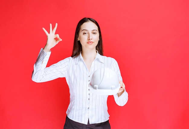 Photo of a beautiful business woman holding safety hat and showing ok gesture.