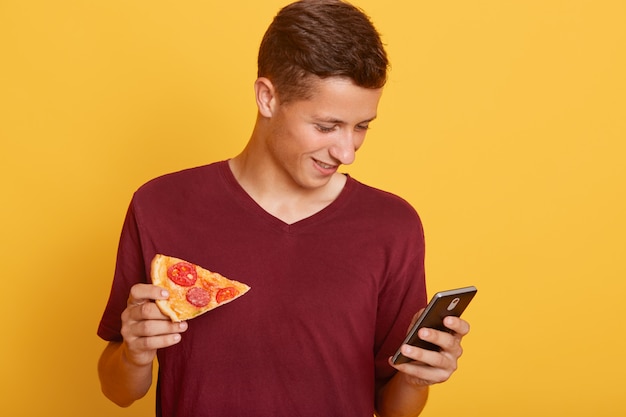 Photo of busy curious joyful teenager holding his smartphone, using his device, checking social networking sites