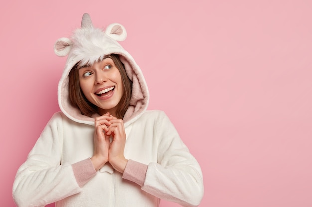 Free photo photo of cheerful dreamy girl keeps hands together, focused upwards with thoughtful glad facial expression