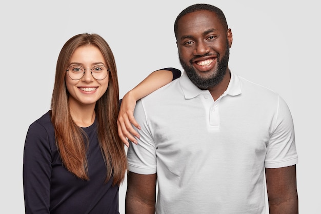 Photo of cheerful lovely diverse couple smile positively, stand next to each other