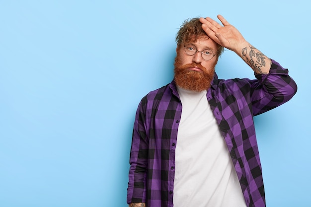 Free photo photo of dissatisfied stylish ginger guy posing against the blue wall