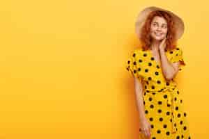 Free photo photo of dreamy lovely redhead woman posing in yellow polka dress and straw hat