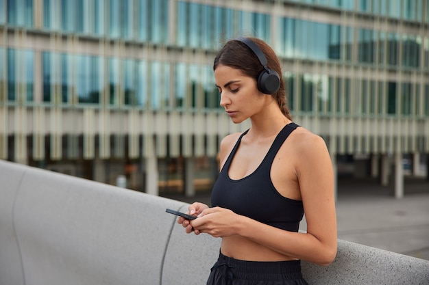 Free photo photo of fit female model chooses song for workout downloads song for her running playlist has break after training wears sportswear poses in modern setting