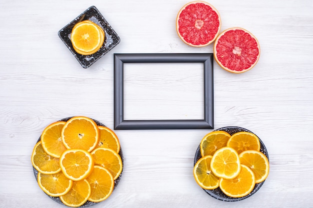 Free Photo photo frame surrounded with orange slices in black plate and two slice of grapefruit on wooden  surface