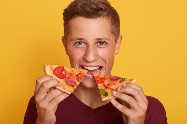 Free Photo photo of guy dressed in burgundy t shirt holding two pieces of pizza and eats fast food