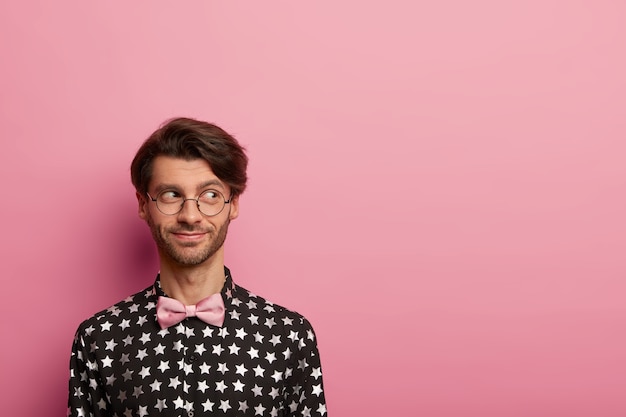 Photo of handsome cheerful man with trendy hairstyle, looks aside, wears optical glasses