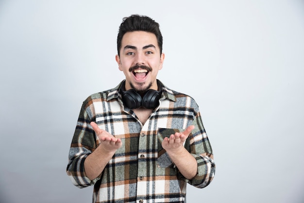 Photo of handsome man with headphones standing and looking over white wall.