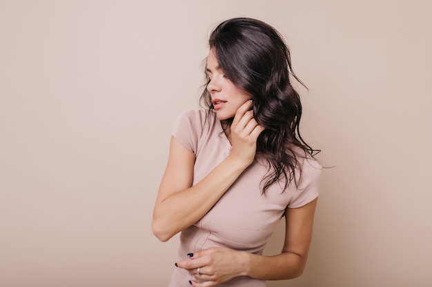 Photo indoors of tanned lady with blue manicure. Girl with wavy shiny hair posing in profile.