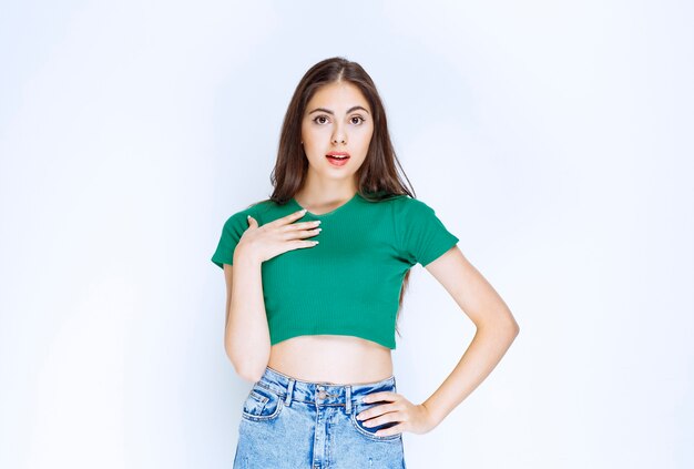 Photo of a lovely girl model standing and looking at camera against white wall.