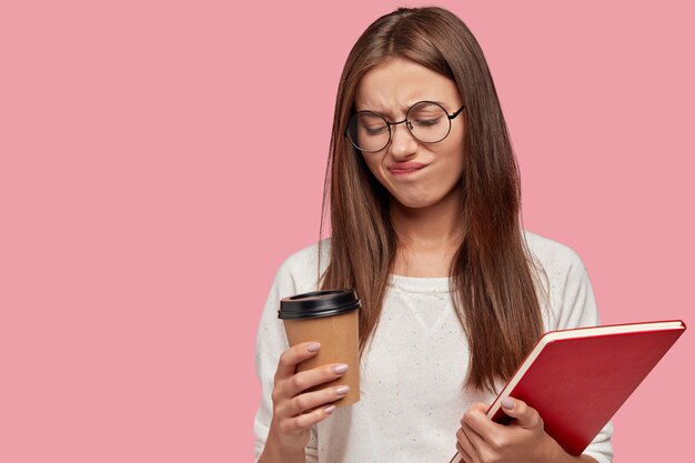 Photo of pretty dark haired woman frowns face in displeasure holds takeaway coffee