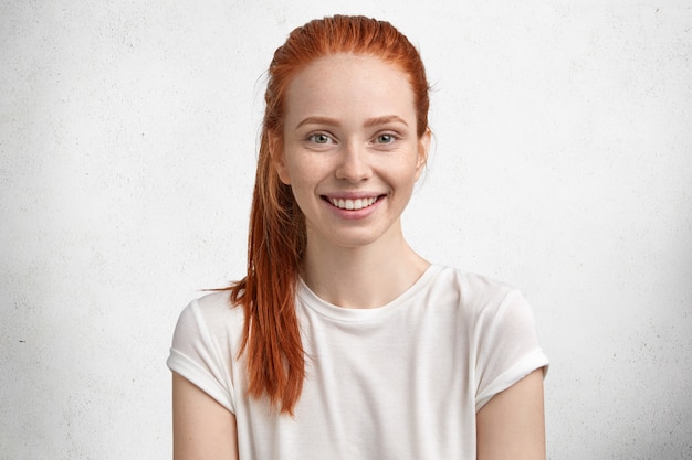 Free photo photo of pretty satisfied ginger female, has green eyes, freckled skin, smiles pleasantly, being in high spirit as spends free time in family circle