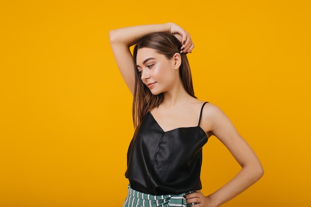 Free photo photo of refined brown-haired girl isolated. portrait of stunning serious caucasian woman posing in black tank-top.