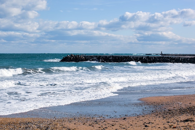 Photo of relaxing ocean waves at the shore with  stone dock under cloudy skies