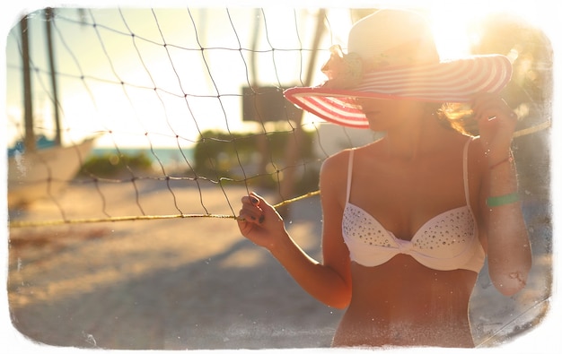 Free Photo photo in retro style  of sexy model girl in white bikini with volleyball net on beach and palms behind blue summer sky