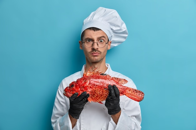 Free photo photo of serious male cook carries fish looks directly at camera asks chef for advice what better to prepare tries tasty yummy recipe