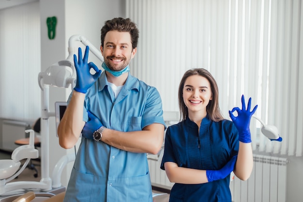 Free photo photo of smiling dentist standing with arms crossed with her colleague, showing okay sign.