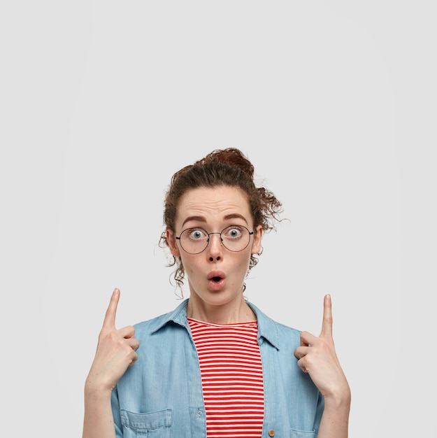 Free photo photo of stupefied emotive freckled woman with dark hair, wears round spectacles