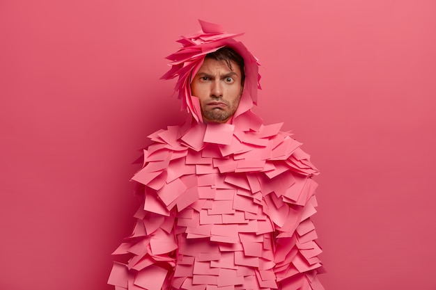 Free Photo photo of sullen displeased european man raises eyebrows, has gloomy face expression, makes unhappy grimace, wears rosy stickers around, discontent with something, isolated over pink wall