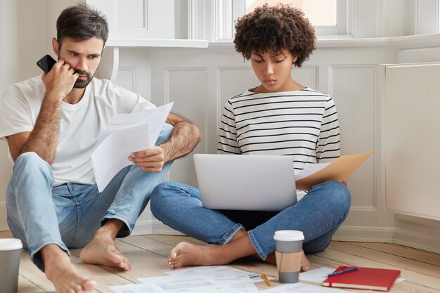 Photo of two mixed race coworkers read documentation, concentrated on solving problem with planning