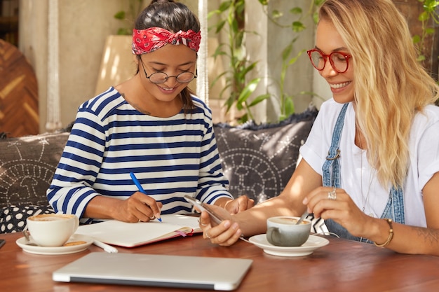 Photo of two multiethnic women sit together at coffee shop