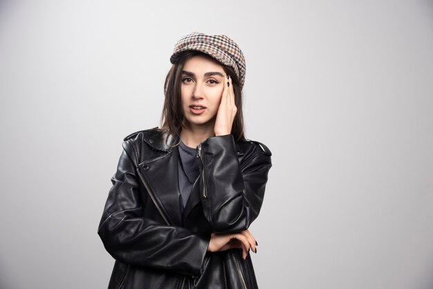 Photo of a woman touching her head in black leather jacket and cap.