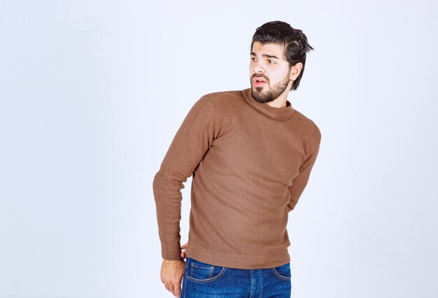 Photo of a young attractive man model standing and looking away over white wall. High quality photo