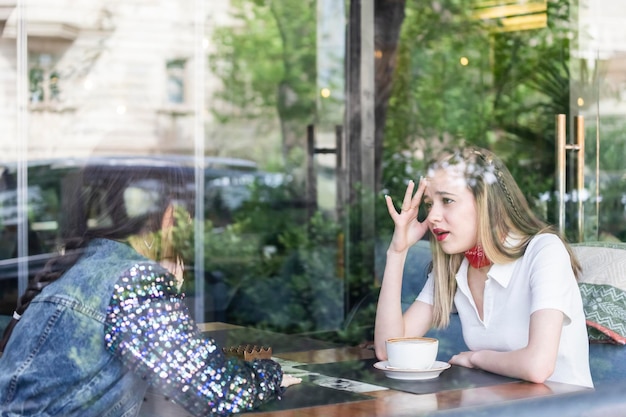 Photo of young beautiful lady sitting at the restaurant and talking with her friend