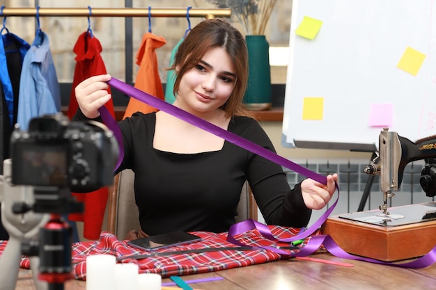 Photo of young female tailor holding purple ribbon and looking at the camera