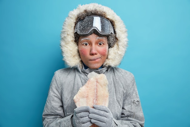 Free Photo photo of young frozen woman with red face wears warm jacket for cold winter conditions holds fillet of fish needs warmth.