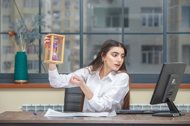 Photo of young lady holding hourglass and looking at the pc