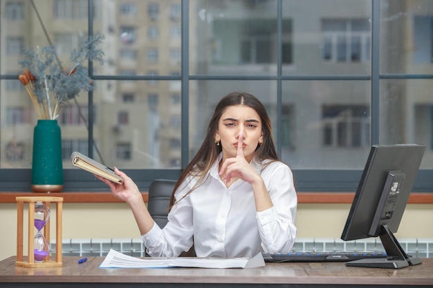 Photo of young lady sitting at the desk and gesture silent