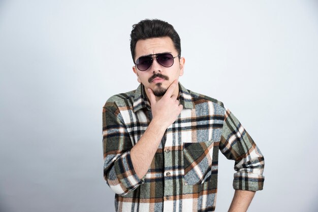 Photo of young man in black glasses standing on white wall.