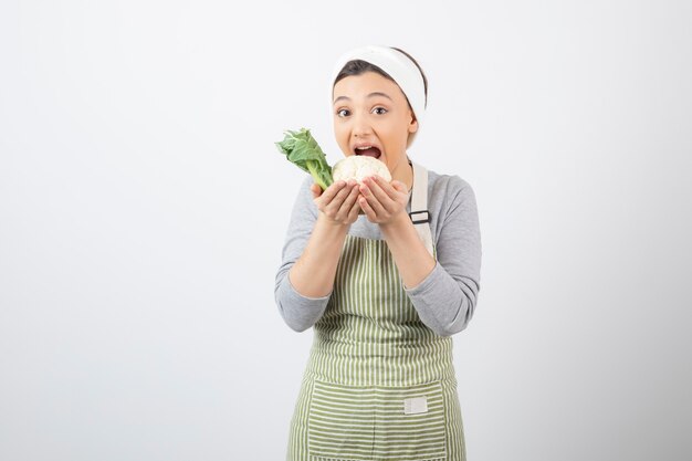 Photo of a young nice woman model in apron eating a cauliflower 