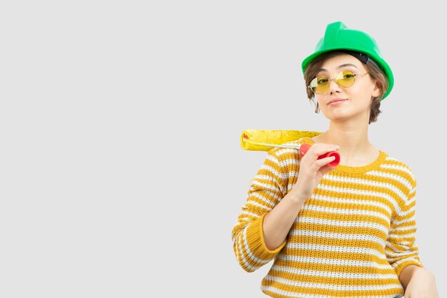 Photo of young woman in green safety helmet holding a paint roller in her hand . High quality photo