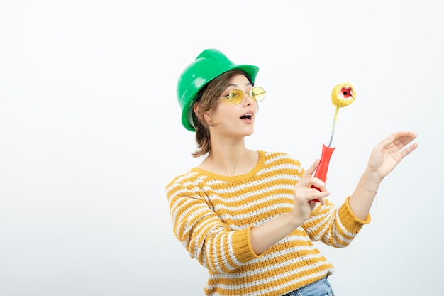 Photo of young woman in green safety helmet holding a paint roller in her hand . High quality photo