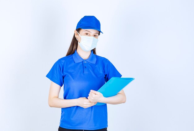 Photo of young woman in medical mask standing and holding folder. 