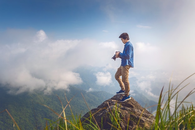 Photographer hand holding camera and standing on top of the rock in nature. Travel concept. Vintage tone.