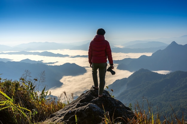 Photographer hand holding camera and standing on top of the rock in nature. Travel concept.